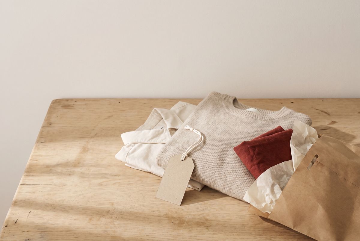 Un pull et une chemise pliés avec une étiquette vierge, à côté d’une enveloppe kraft sur une table en bois